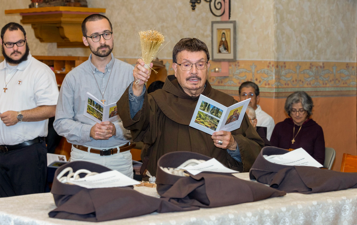 A Franciscan friar blesses three habits with holy water