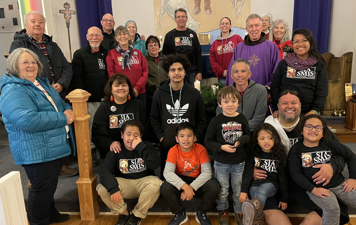 A group of 22 people of all ages with a priest wearing purple robes