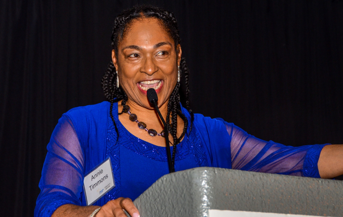 A Black woman in a blue dress gives a speech at a podium