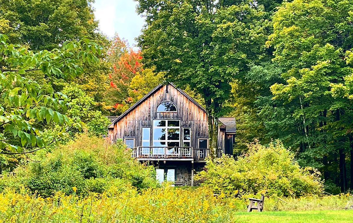 A chapel with large windows nestled in the woods overlooking a meadow