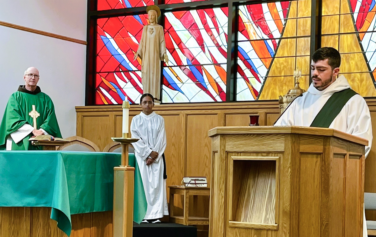 A young friar wearing the white robes of a deacon proclaims the Gospel during a Catholic Mass