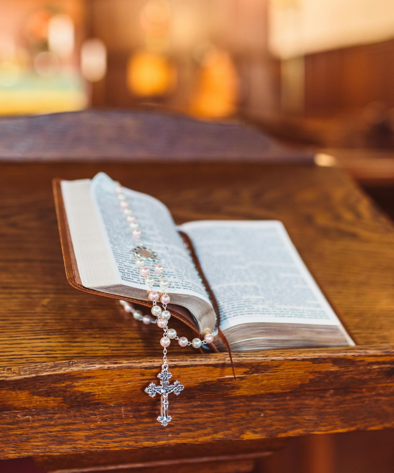 A bible sits on a podium with a rosary wrapped around one side of it.