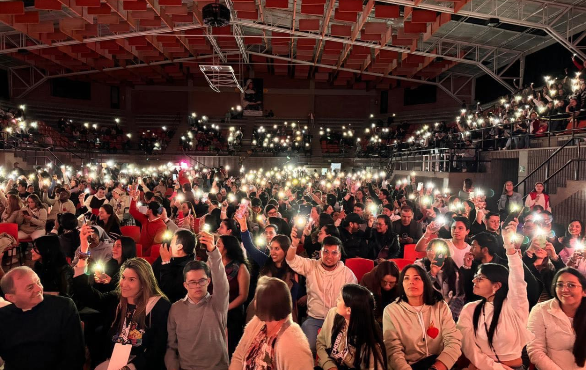 Dozens of young people hold up lights during a conference festival in an arena.