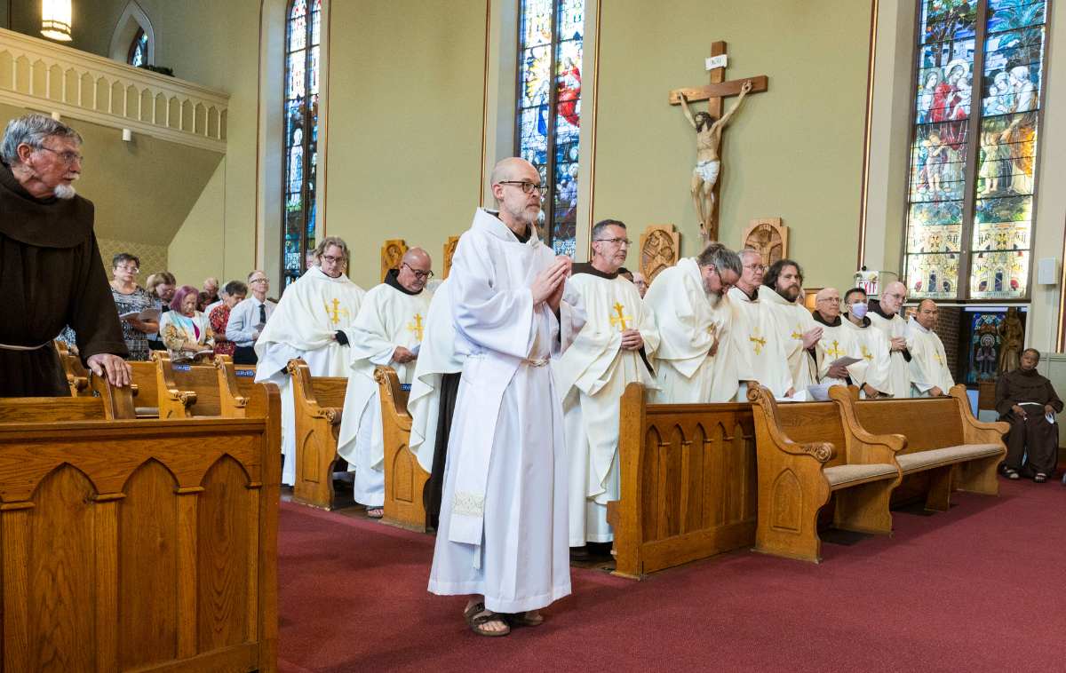 A man stands before a church congregation with hands folded in prayer.