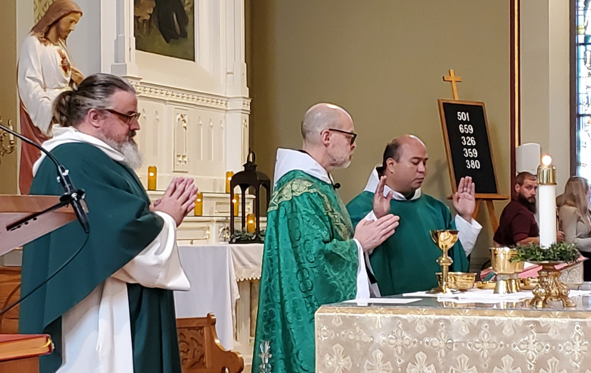 A priest gives Mass in a Catholic church. Two other clergy are standing with him at the altar.