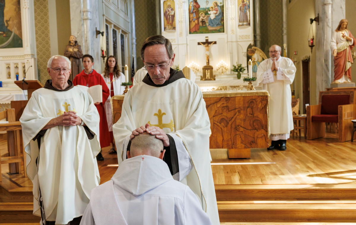 A priest lays hands on a man's head in prayer.