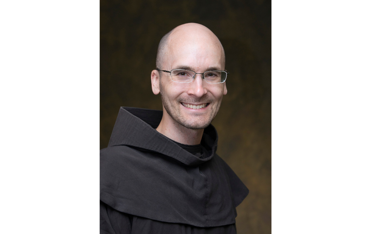 A man wearing glasses and smiling wearing a friar habit.