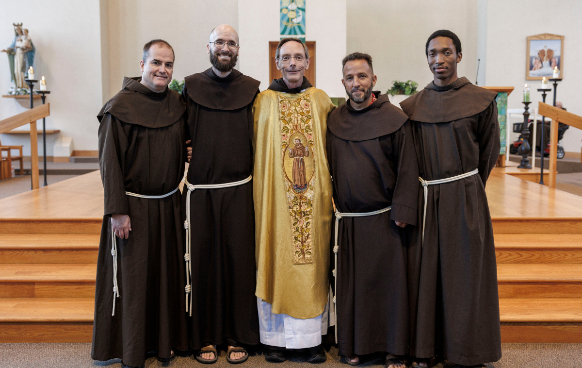 The four solemnly professed friars stand with Larry Hayes at the front of the church. All five men are smiling at the camera.