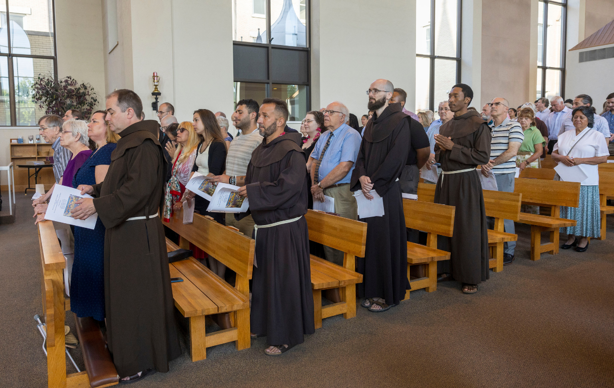 A line of Franciscan friars wearing brown habits process into a church.