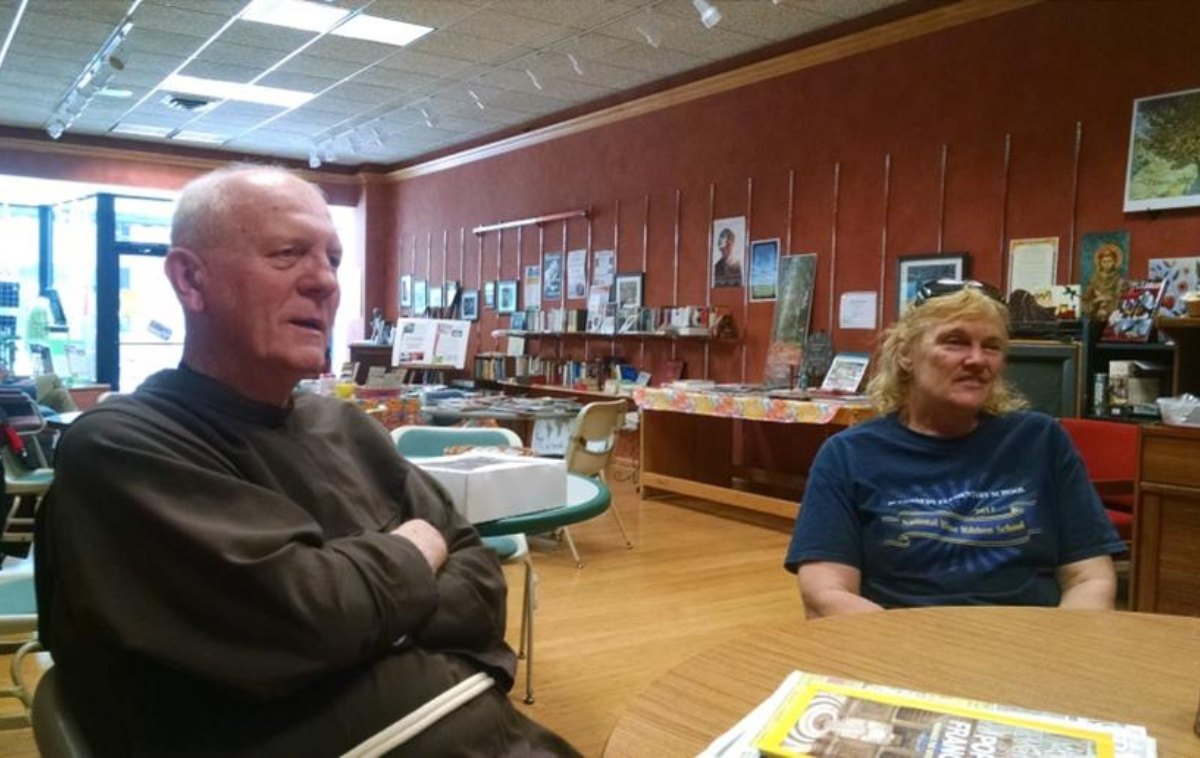 A friar sits next to a visitor at a round table