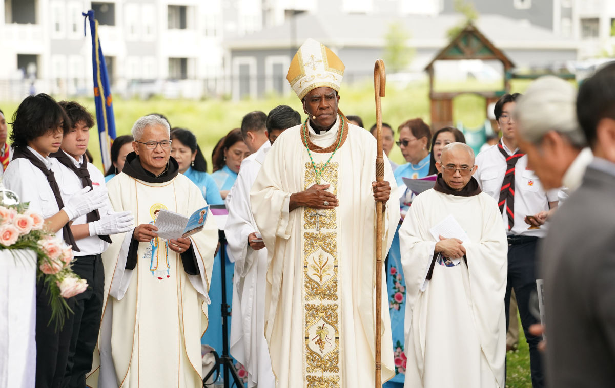 Br. David Phan, wearing white vestments, stands among a crowd of people who are praying. To his left are Bishop Jacques Fabre-Jeune, CS, and Br. John Tran Nguyen, a fellow Vietnamese friar.