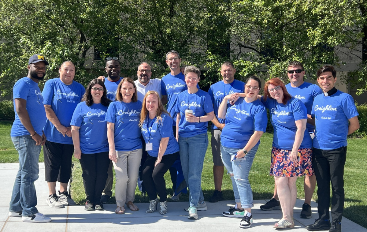 Br. Moises stands among 14 people wearing bright blue shirts with 