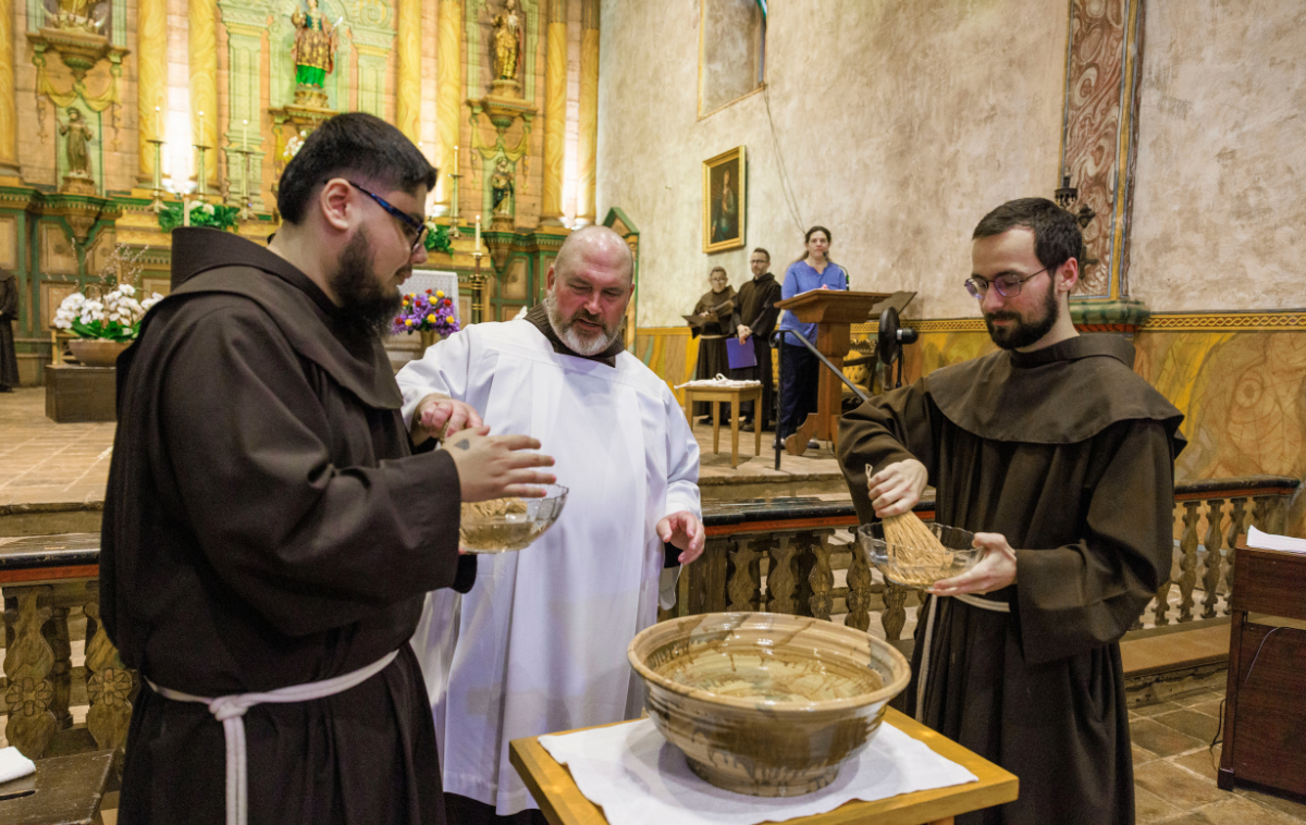 Two young friars pick up glass bowls of water and brushes so that they may bless attendees with holy water.