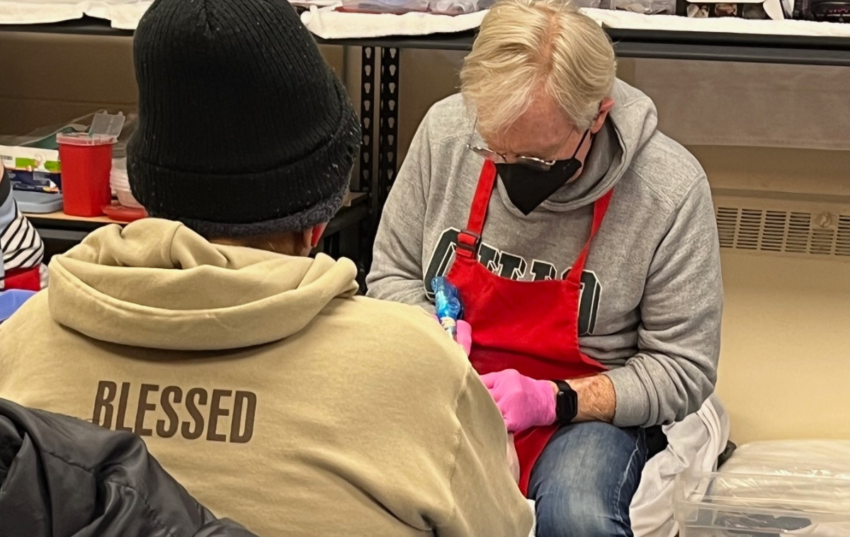 A man wearing pink gloves and a red apron over his clothes provides care for a guest's foot