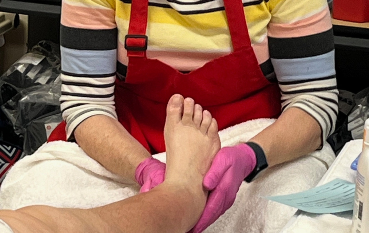A volunteer wearing pink gloves and a red apron cares for the foot of a guest