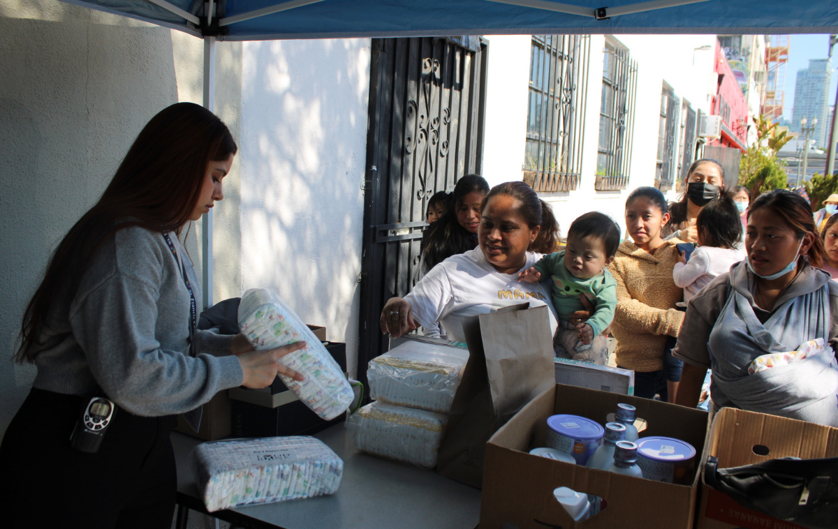 A person distributes packages of diapers to waiting families and their children