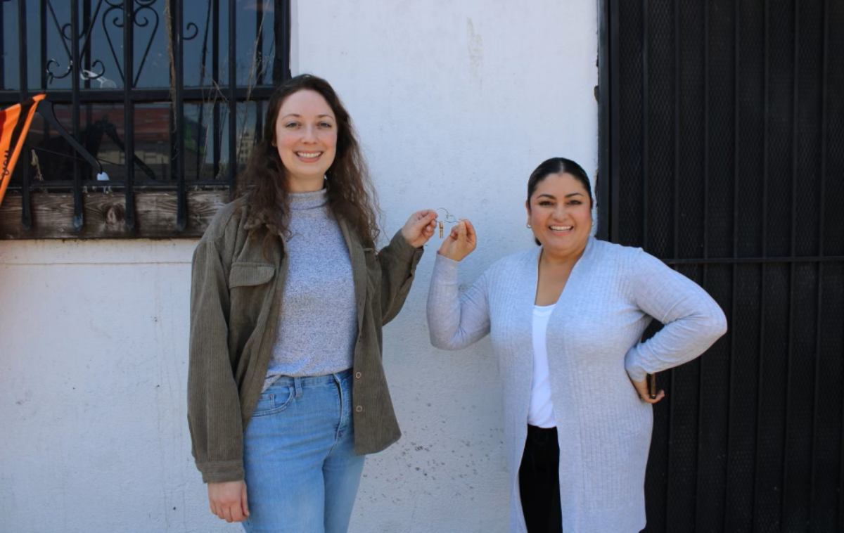 Two smiling people hold up the key to a building. They are standing in front of a white concrete wall.