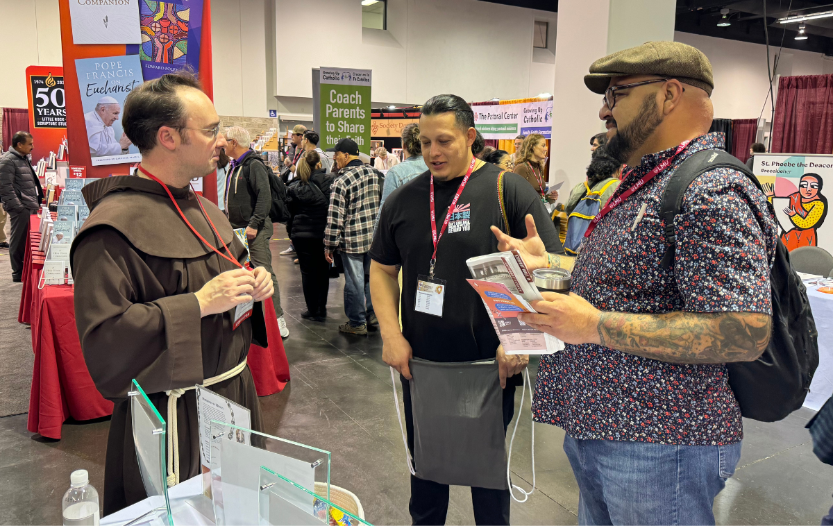 A friar welcomes two people to the friars' booth at RE Congress