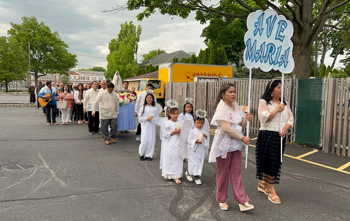 A group of people process toward a church led by two women carrying a sign that reads 