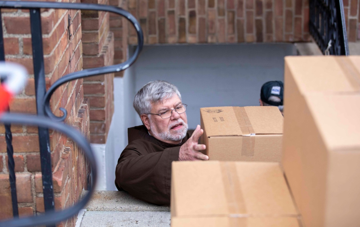 A friar stacks a pile of cardboard boxes filled with canned goods.