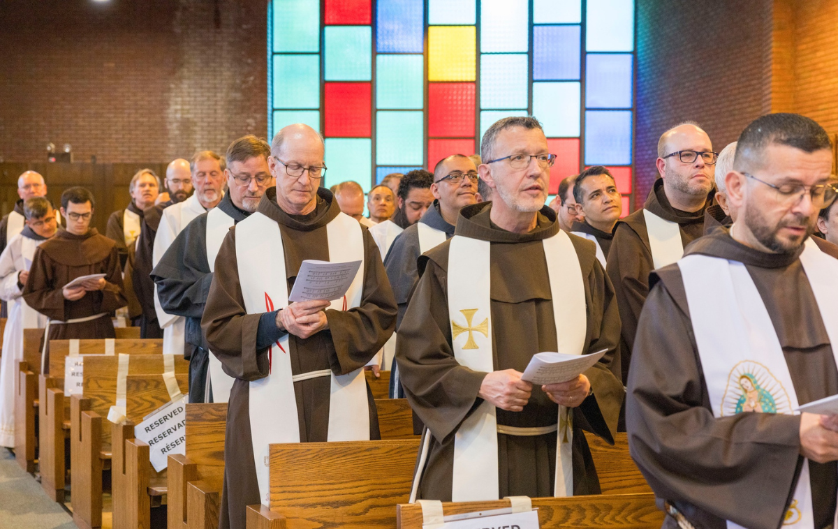 Franciscan friars stand in the pews of a church and look toward the altar