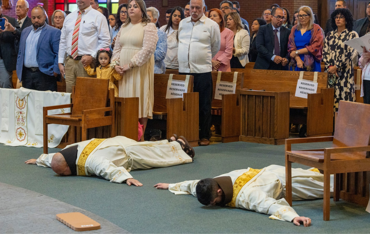 Two friars lie prostrate on the floor of a church.