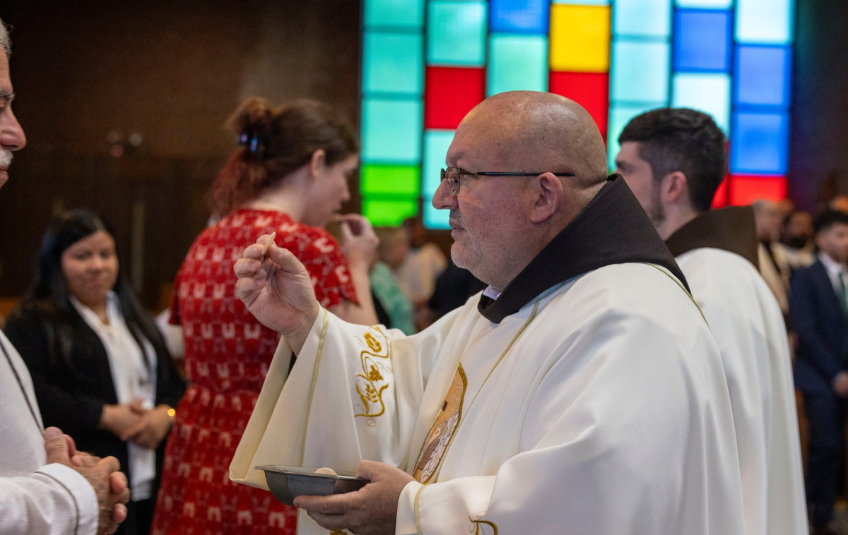 A friar-priest gives Communion to a guest at the ordination
