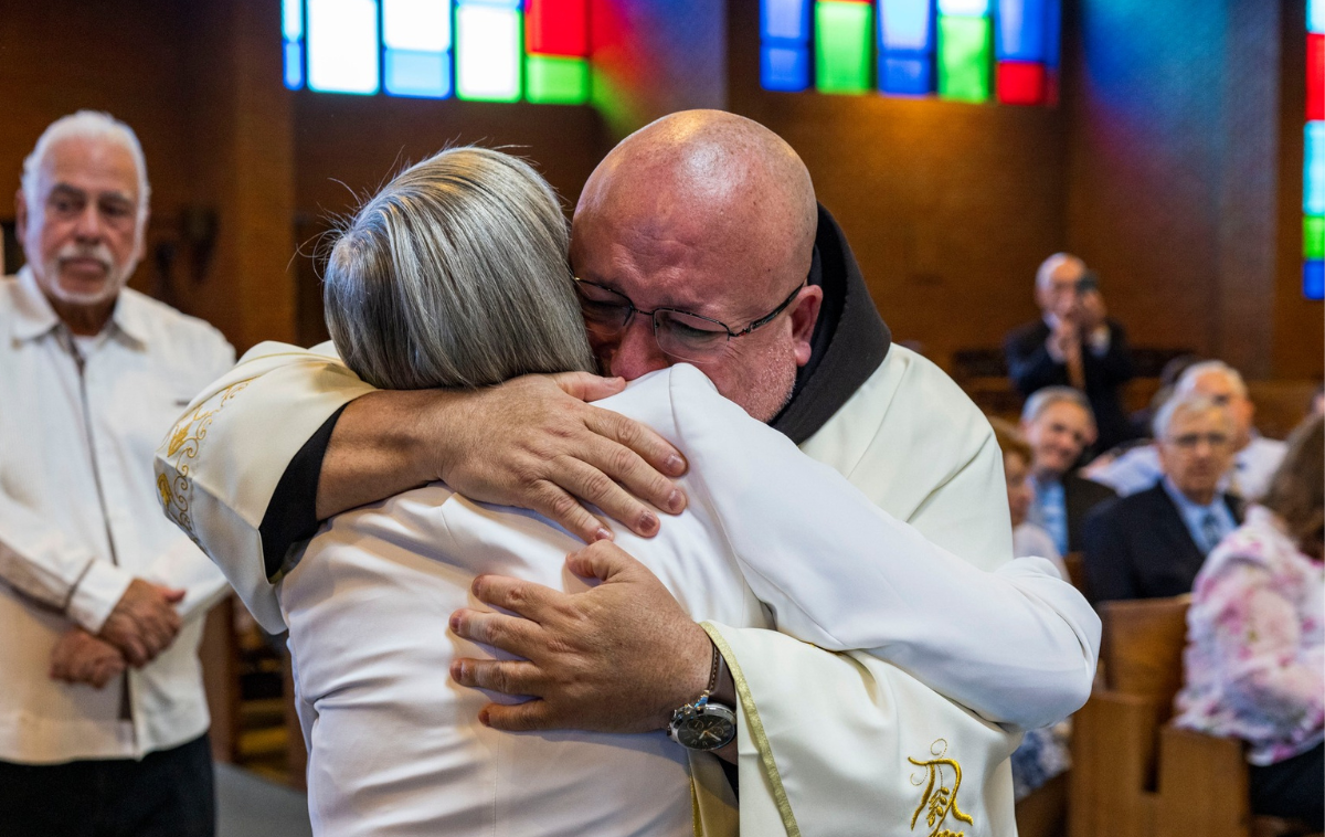 A friar-priest hugs his aunt with a tearfully joyful look on his face.