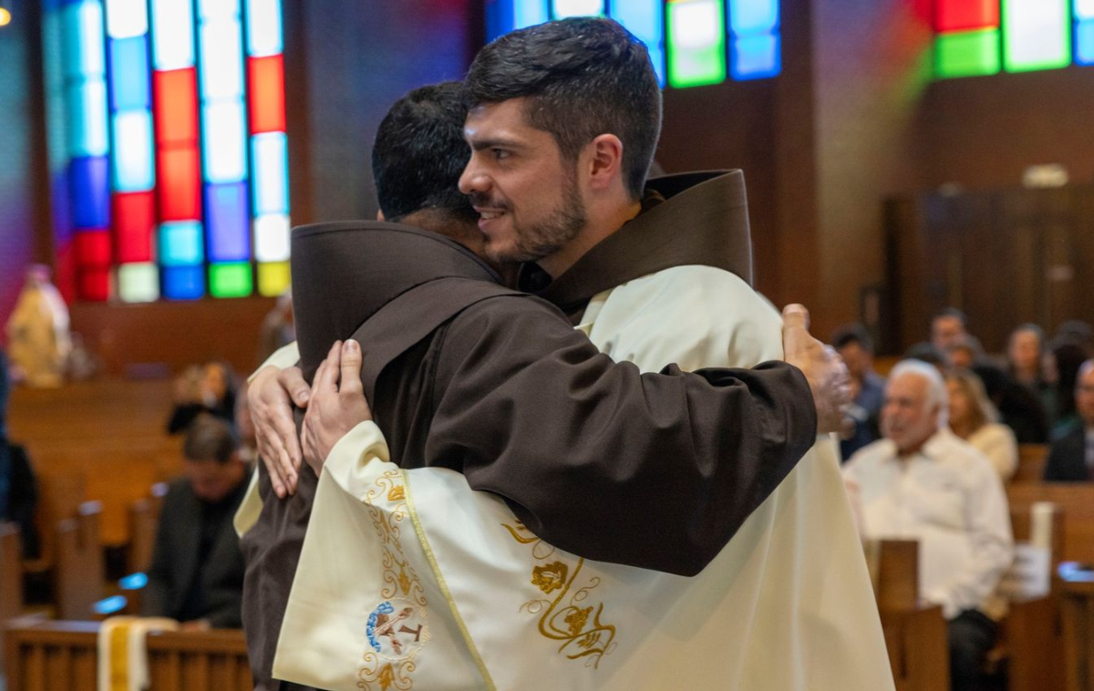 A friar-priest receives a hug from another friar.