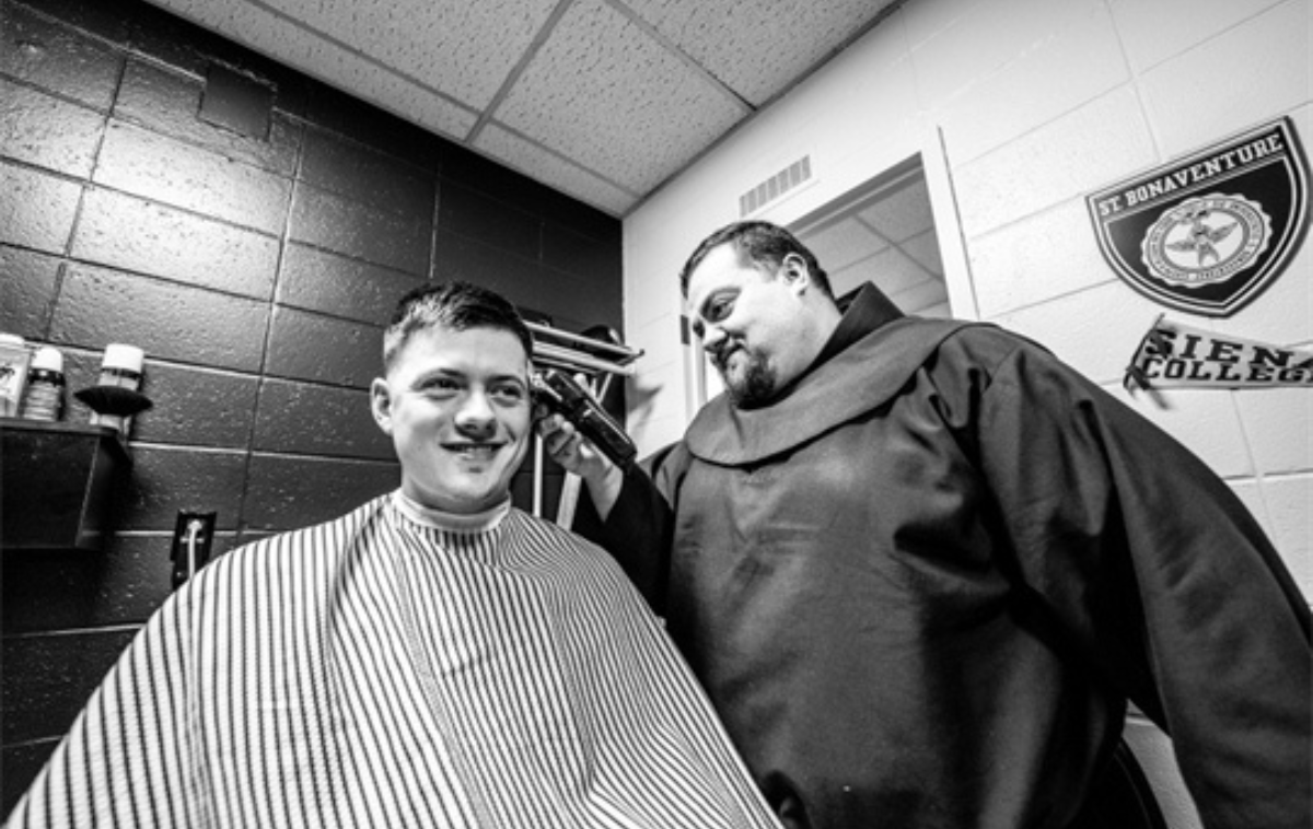 A friar trims the hair of a man sitting in a barber's chair.