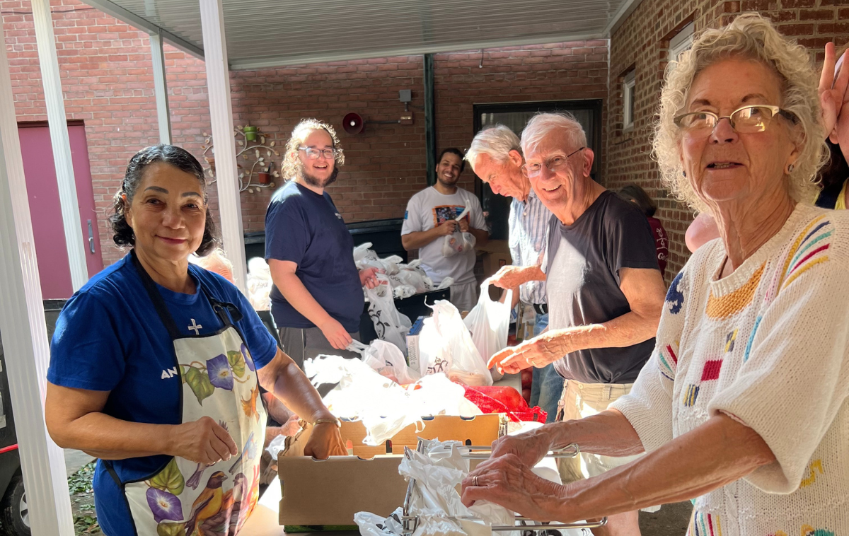 A group of six smiling people pack grocery bags with food.