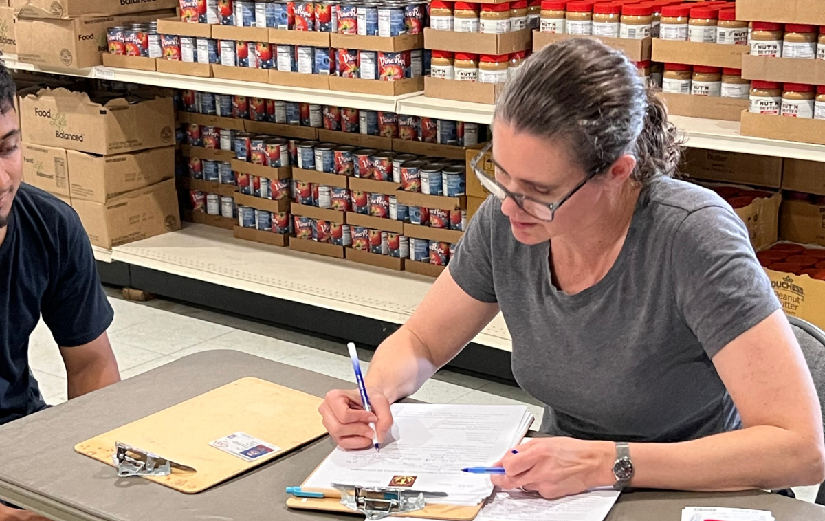 A woman in a grey shirt helps a man complete a form.