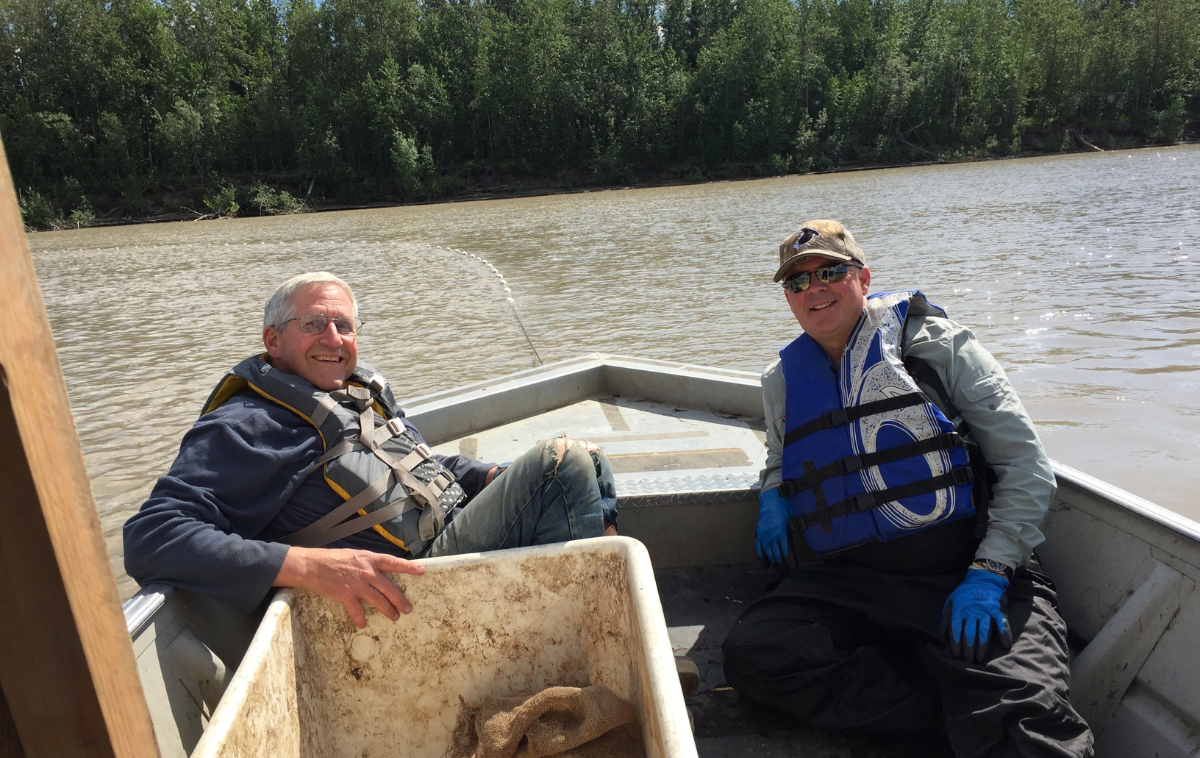 Two men wearing life jackets sit in a small boat.