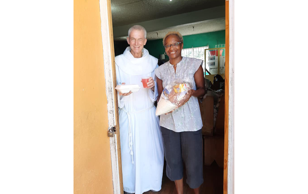 Jim, who is wearing a white Franciscan habit, stands in the doorway of St. Anthony's Kitchen next to a smiling parishioner who is holding a large loaf of bread.