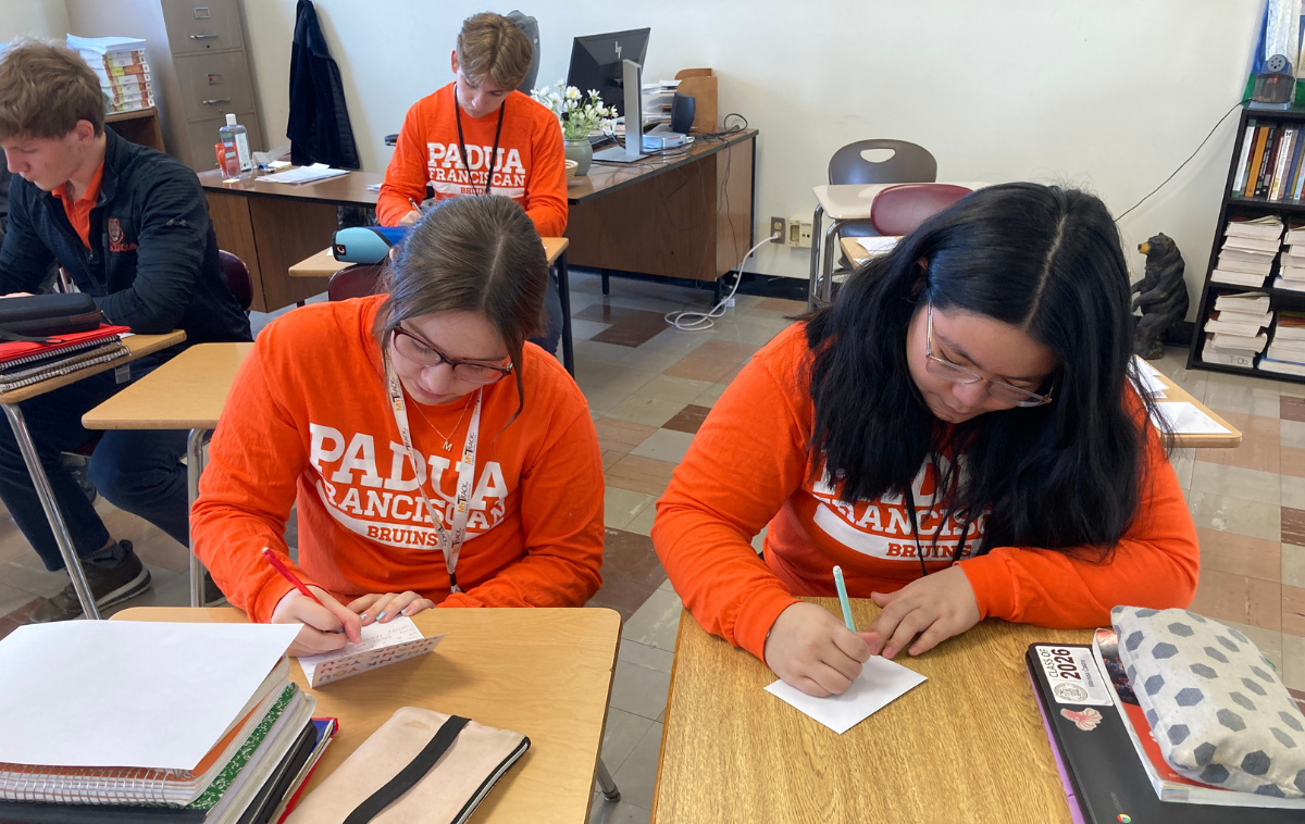 Students wearing bright orange 'Parma' shirts write thank you notes at their desks.