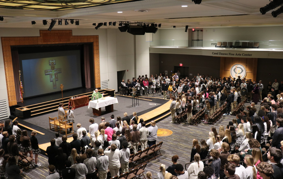 A friar celebrates Mass in an auditorium full of children.