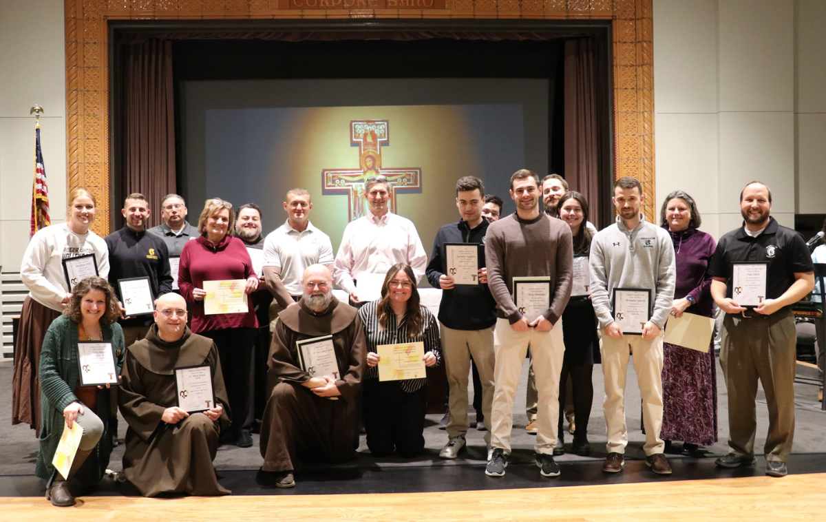 20 faculty members hold up certificates that celebrate their achievements.