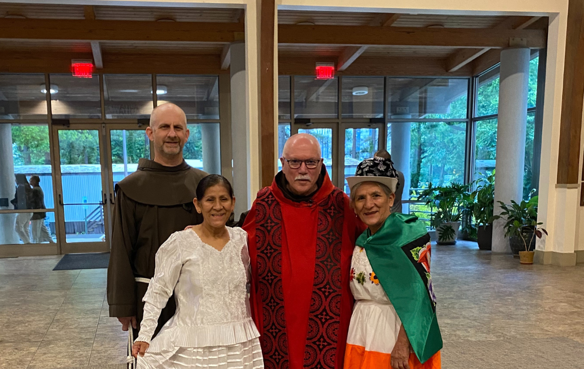 Two friars stand with two women dressed in traditional Mexican costumes.