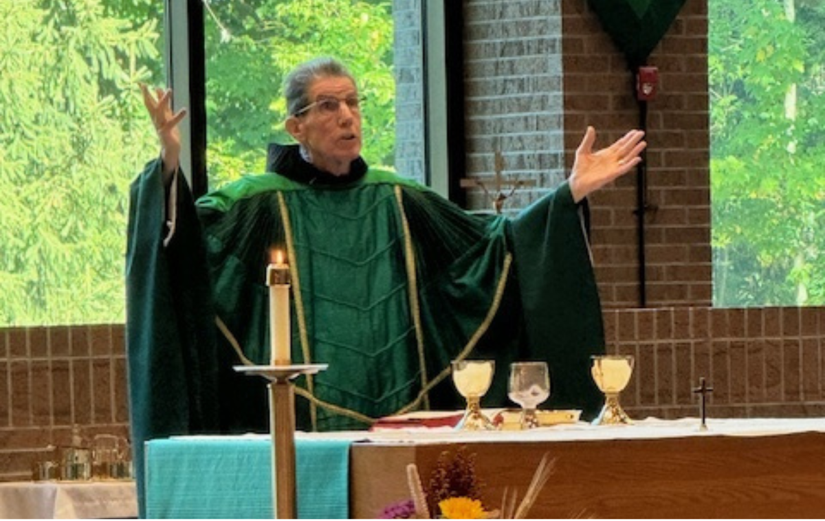 A friar wearing green vestments elevates the host.