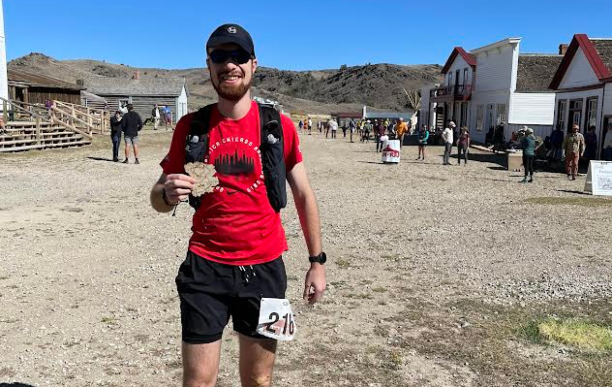 A young friar standing in a desert town holds up a marathon medal