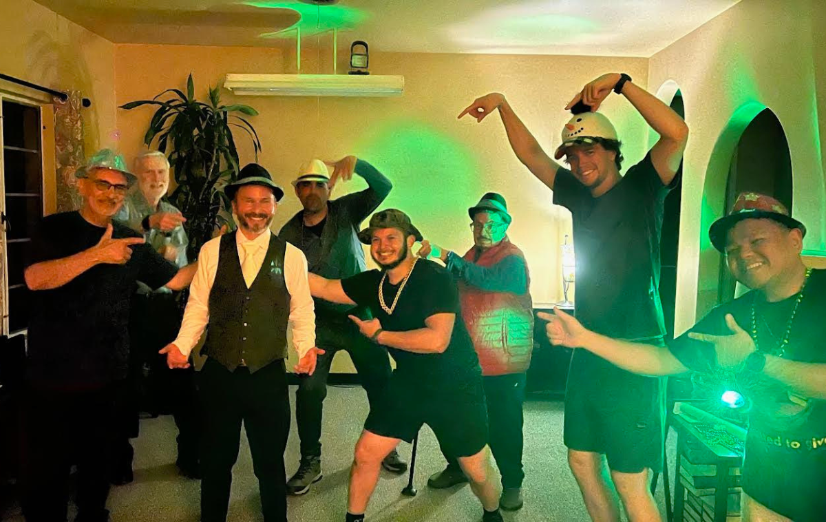 A group of eight smiling friars wearing fedoras pose for a photo