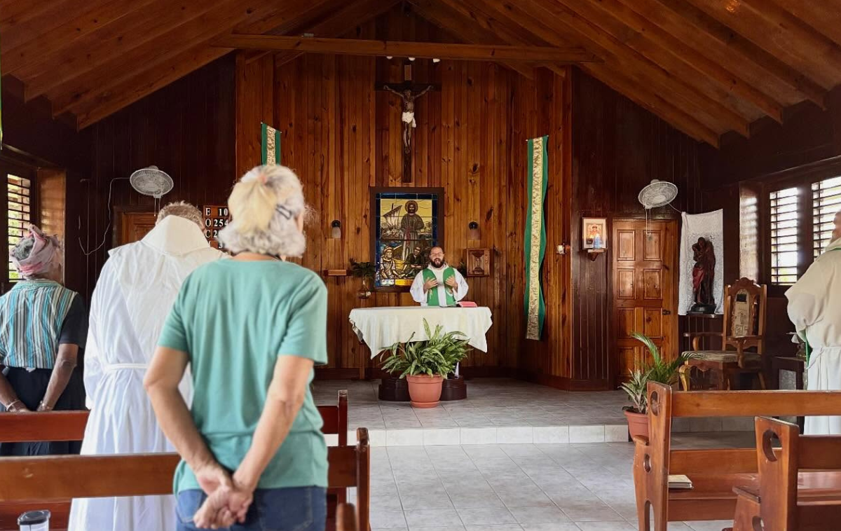 A friar welcomes three people who are picking up bags of food.