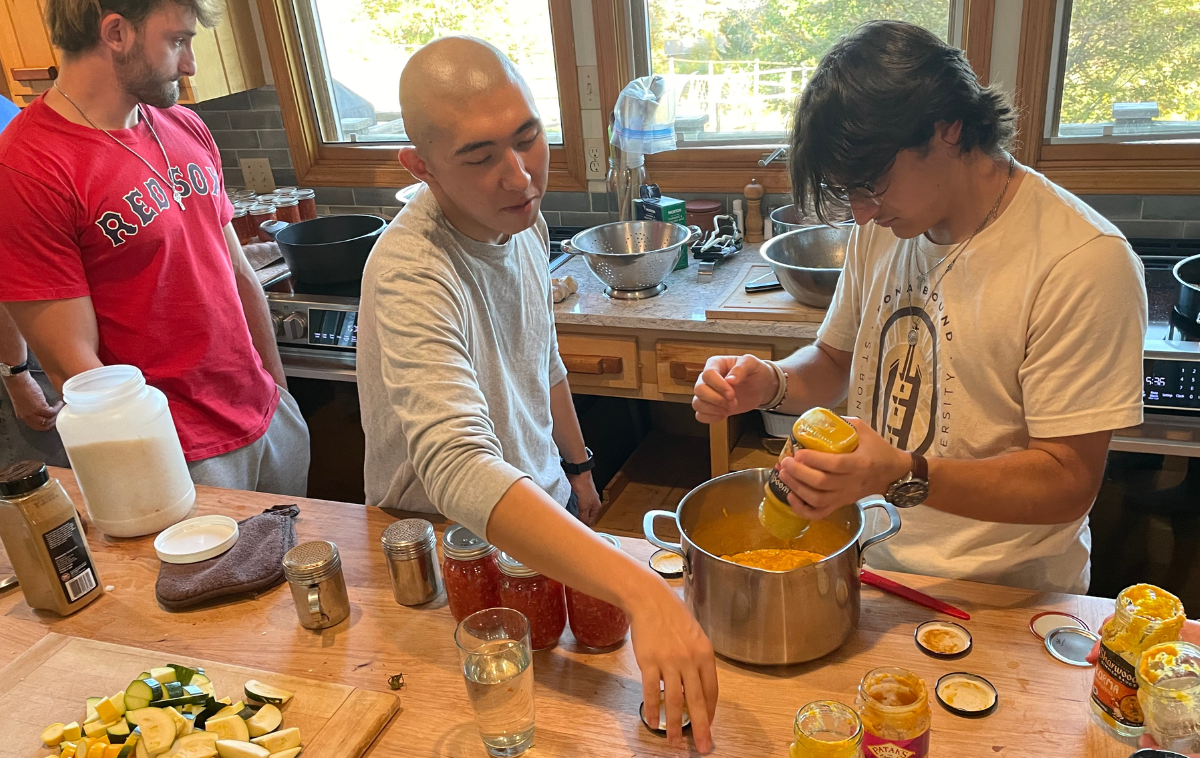 A friar welcomes three people who are picking up bags of food.