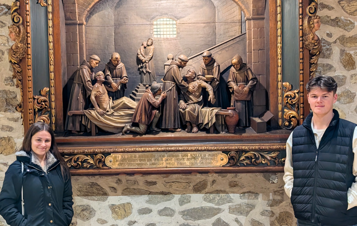 Siena students stand next to an image of Francis and his brothers caring for the lepers. (Photo courtesy of Siena University)&nbsp;