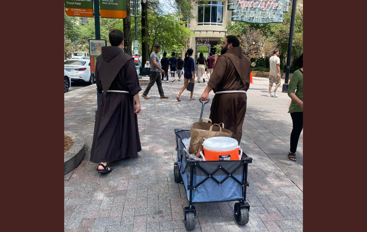 Several days a week, the friars walk the streets of Uptown Charlotte with a wagon of ice-cold water and peanut butter and jelly sandwiches prepared by parishioners of St. Peter Catholic Church. Earlier that afternoon, one man waved over Brothers Casey and Tito for water and candy. "I love it when y'all come out," he said. "I get my favorite snack: peanut butter and jelly." (Photo by Eli Pacheco)