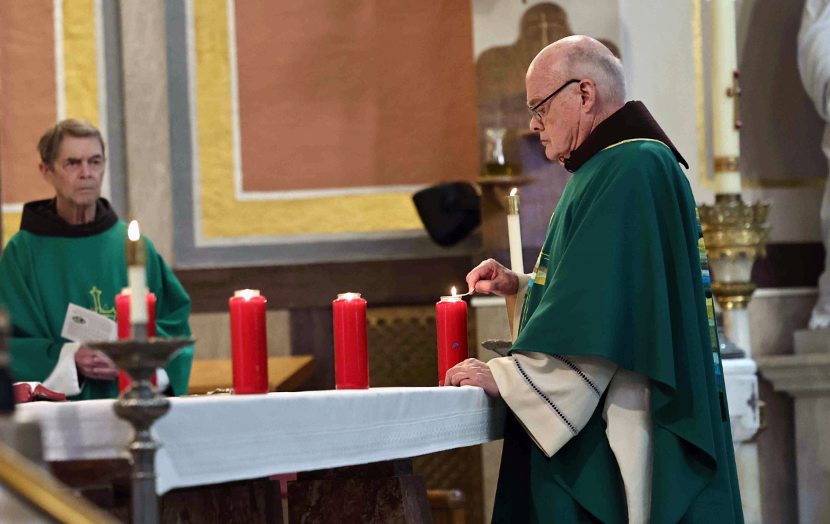 A priest lights a candle on the altar as another watches