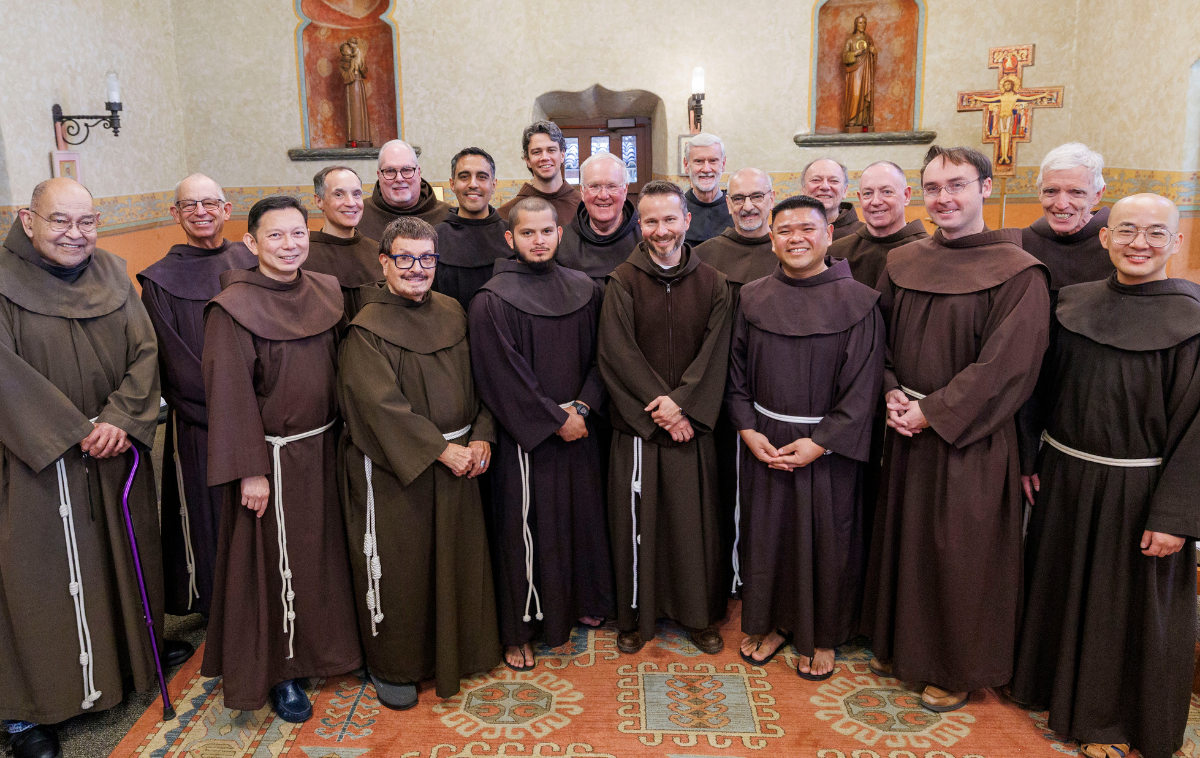 Nineteen men wearing friar habits pose for a photo.