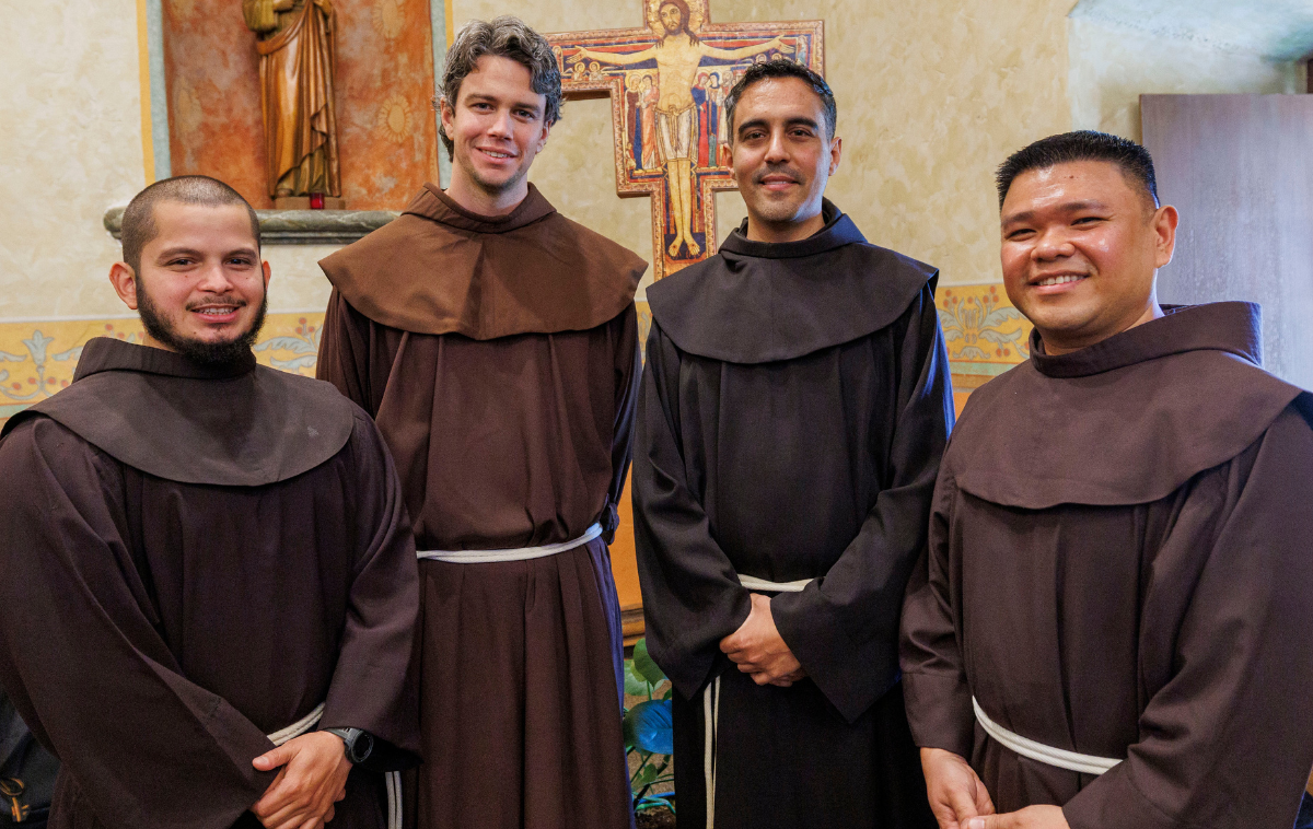 Four smiling men in friar habits pose for a photo.