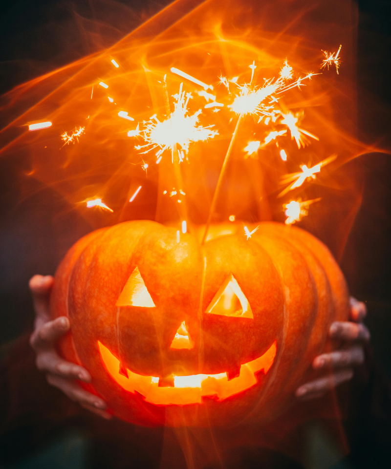 Lights inside and sparklers on top illuminate a jack-o-lantern held by two hands.